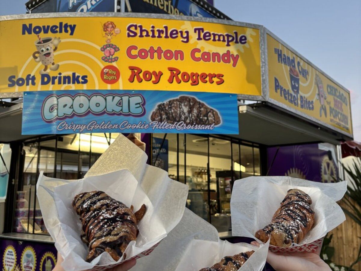 The Sweet & Salty stand at The Big E, with signs for novelty soft drinks, cotton candy, and Crookies, and two chocolate-drizzled crookies held up in front of it.